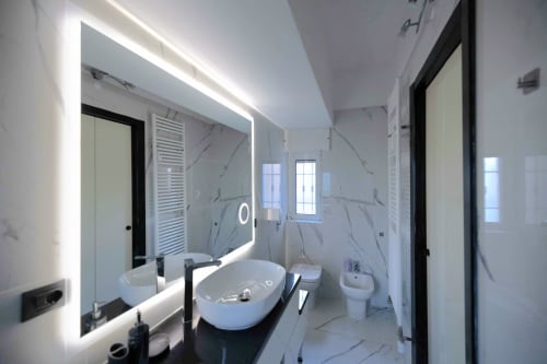 Modern bathroom with marble walls, illuminated mirror, and white vessel sink in Milano apartment
