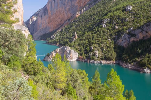 Turquoise lake surrounded by steep rocky cliffs and pine forest near El Pont de Suert, Spain