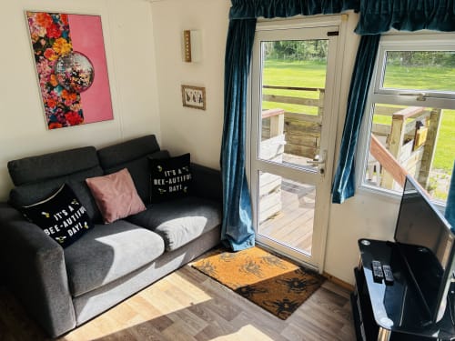 Cozy living area in Two-Bedroom Owl Country Cabin at Postwood Gardens with black sofa, floral artwork, and garden views
