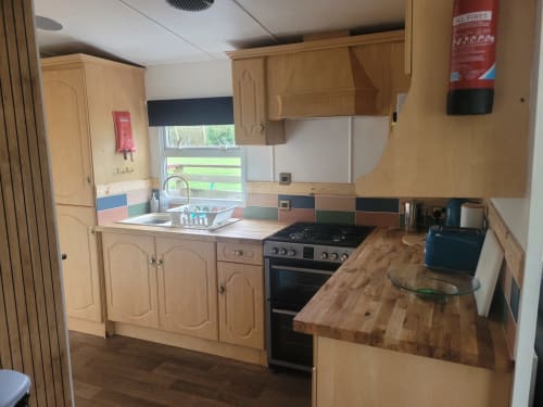 Modern kitchen in Two-Bedroom Owl Country Cabin at Postwood Gardens Campsite, Kentisbeare with wooden cabinets, black stove,