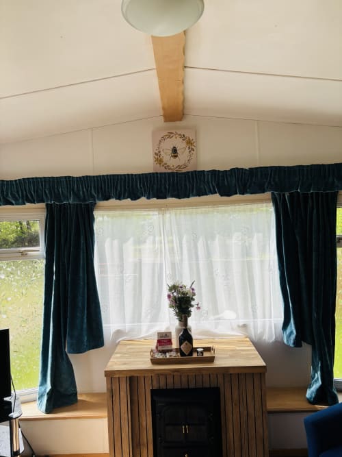 Cozy cabin sitting area with wood fireplace, dark teal curtains, white sheer drapes, and garden views at Postwood Gardens