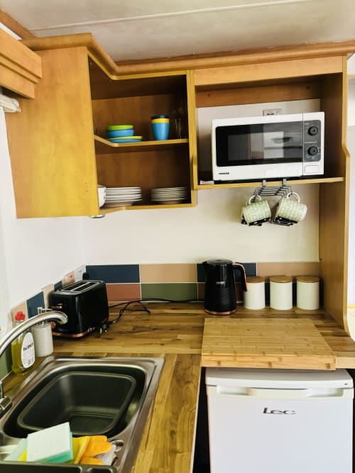 Compact kitchen area in Three-Bedroom Fox Country Cabin with wooden cabinets, microwave, toaster, kettle, and sink at