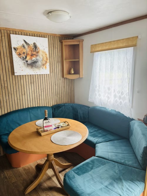 Cozy dining seating area in Fox Country Cabin at Postwood Gardens Campsite with teal sofa, round wooden table, and fox