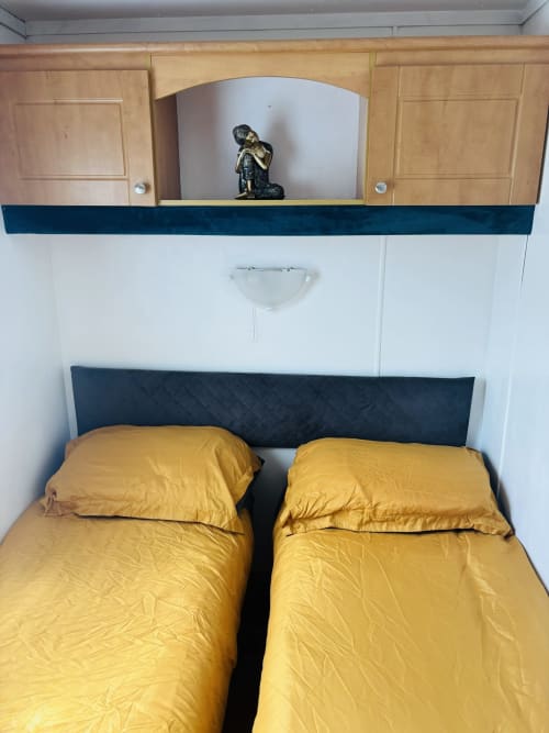 Twin beds with yellow bedding in modern cabin bedroom with dark headboard, wooden cabinets, and storage niche at Postwood