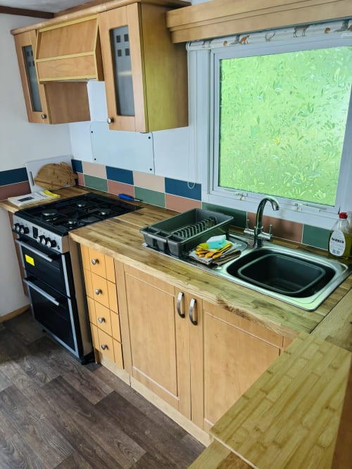 Kitchen in Three-Bedroom Fox Country Cabin at Postwood Gardens Campsite with gas range, wooden cabinets, sink, and garden