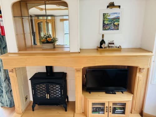 Cozy cabin living area with wooden mantel, black fireplace stove, built-in TV unit, and garden view artwork at Postwood