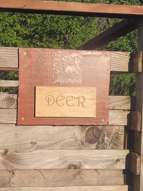 Wooden sign reading 'DEER' mounted on rustic cabin exterior at Postwood Gardens Campsite, Kentisbeare