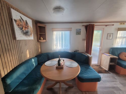 Cozy cabin lounge at Postwood Gardens with teal seating, round dining table, and fox artwork in Kentisbeare
