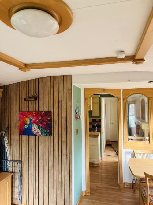 Modern cabin interior at Postwood Gardens with wooden beams, vertical paneling, ceiling light, and colorful peacock artwork