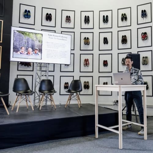 Man presenting at Golden Mermaid Villa event with shoe art display and audience seating backdrop