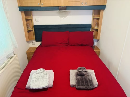 Red bed with dark headboard, folded towels, and wooden nightstands at Postwood Gardens Campsite, Kentisbeare