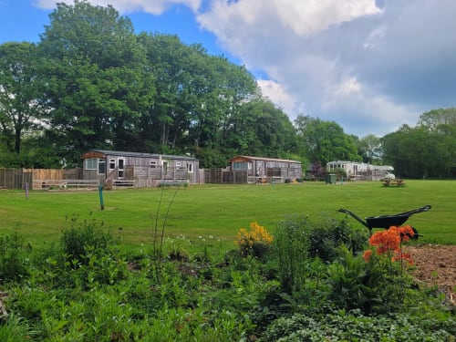 Postwood Gardens Campsite in Kentisbeare with vintage caravans on grassy grounds, colorful flower beds, and trees.