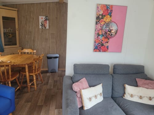 Modern lounge area at Postwood Gardens Campsite with gray sofas, wooden dining table, and floral disco ball artwork
