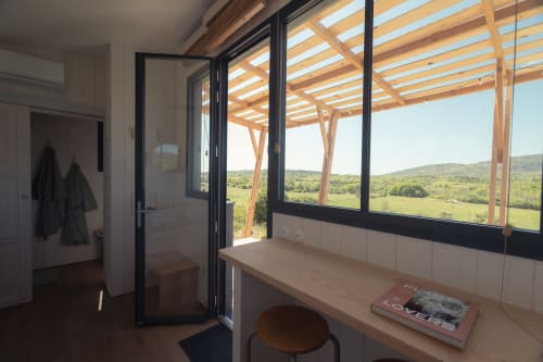 Véranda Pépiite BnB avec pergola en bois, vue panoramique sur la campagne de Villeneuve, banc en bois et magazines