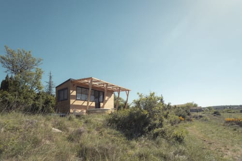 Cabine Pépite BnB à Villeneuve avec pergola en bois, dans un paysage rural avec végétation parsemée et ciel dégagé