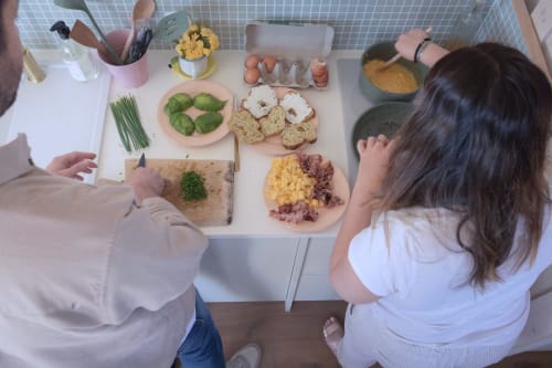 Deux personnes préparant le petit-déjeuner à Pépiite B&B à Villeneuve avec des ingrédients frais et des viennoiseries sur une table blanche