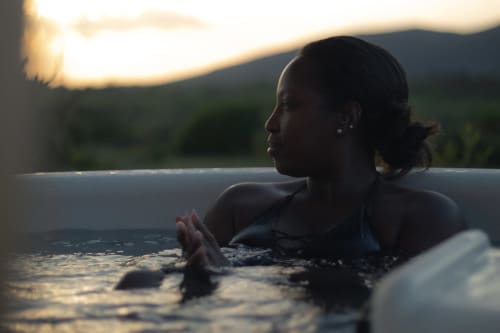 Femme se relaxant dans un bain à remous extérieur au coucher du soleil, gîte Pépiite à Villeneuve avec vue sur les montagnes