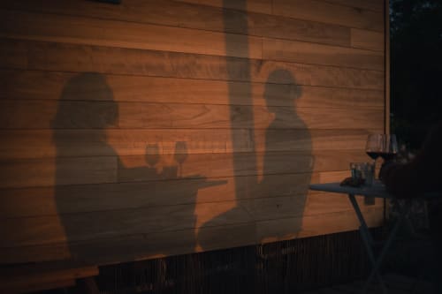 Ombres de clients dînant à Pépite BnB à Villeneuve, France, projetées sur un mur en bois au coucher du soleil