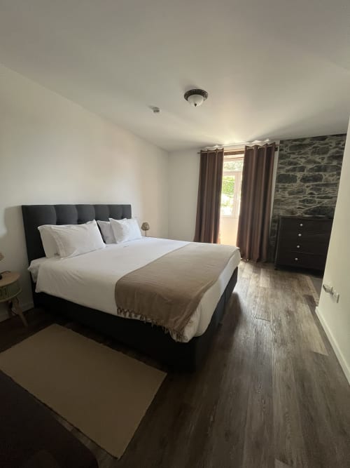 Modern bedroom at The Rum Inn in Calheta, Madeira with queen bed, stone wall, and wood flooring