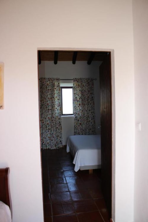 Small bedroom in Monte Da Morena B&B with bed, patterned curtains, window, and dark tiled floor