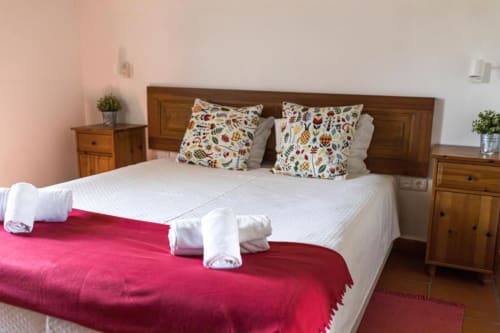 Spacious Superior Double Room at Monte Da Morena with wooden bed, white linens, red throw, colorful pillows, and wooden