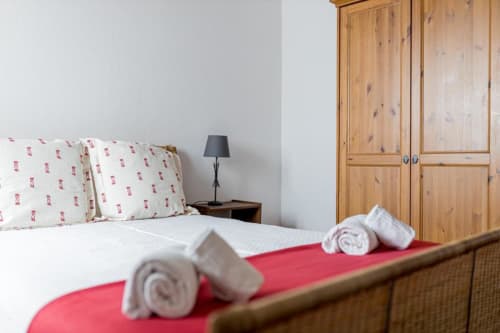 Cozy bedroom with white pillows, rolled towels on red runner, wooden wardrobe at Monte Da Morena Agro-Turismo in Serpa