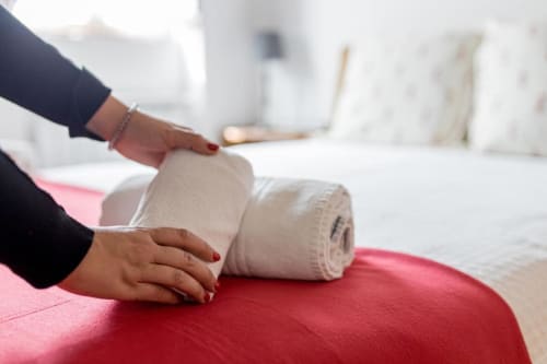 Hand arranging rolled white towels on red bedding at Monte Da Morena Agro-Turismo apartment in Serpa, Portugal