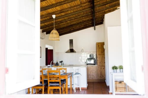 Rustic kitchen and dining area in Monte Da Morena apartment with wooden beams, wicker pendant light, and garden views in