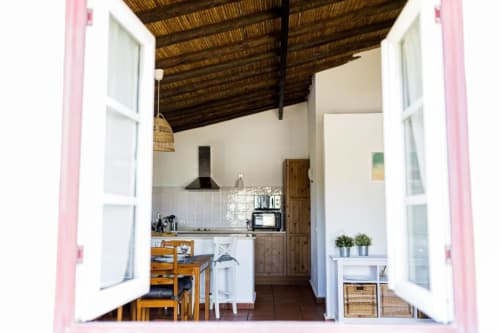 Bright kitchen-dining area in Monte Da Morena apartment with pink doors, wooden beams, and garden view
