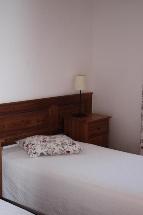 Bedroom with wooden double bed, white linens, floral pillow, and bedside lamp at Monte Da Morena in Serpa