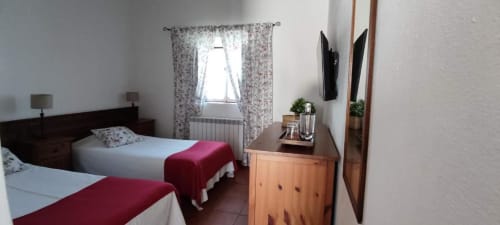 Twin bedroom at Monte Da Morena with white beds, burgundy throws, floral curtains, wooden furniture, and garden view window