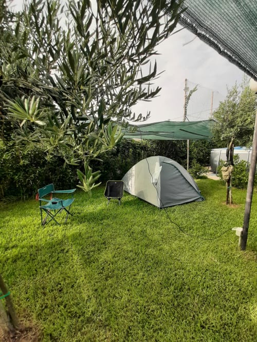 Allestimento di tenda da campeggio su prato verde presso il Baia Dorica Camping Village di Vittoria, Italia, con sedia e tendone ombreggiante