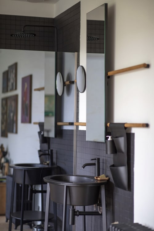 Salle de bain moderne de la Villa Sonneville avec carrelage sombre, miroirs circulaires doubles, porte-serviettes en bois et accessoires noirs