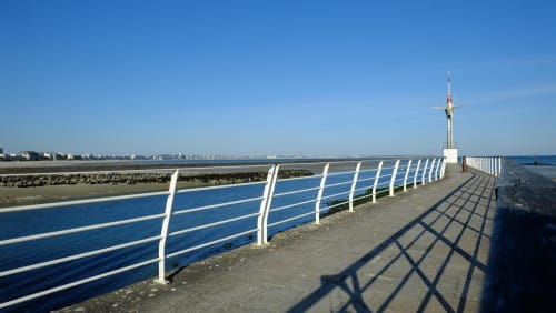 White railing on waterfront pier in La Baule with blue sky and coastal town, Hôtel Amirauté view