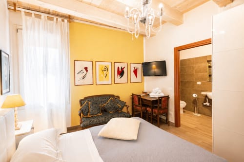 Camera da letto lussuosa all'Al Battistero di Ravenna con parete gialla, letto matrimoniale, divano antico e bagno en suite