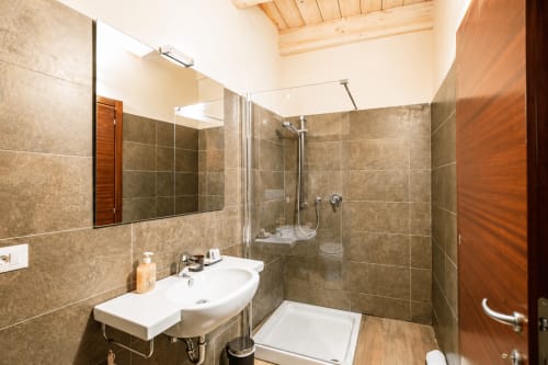 Bagno moderno con doppio lavabo, doccia walk-in e pareti piastrellate presso l'Al Battistero Luxury Suite di Ravenna
