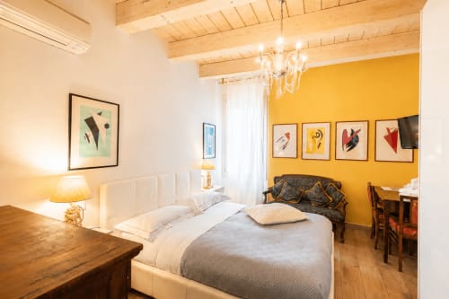 Suite di lusso all'Al Battistero di Ravenna con parete accent gialla, letto bianco, travi in legno e servizi moderni