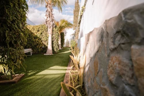 Allée verdoyante de l'Aevum Resort avec palmiers, pelouse soignée et murs en pierre à Playa del Inglés
