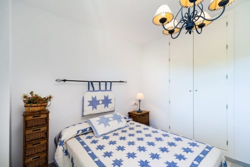 Dormitorio luminoso en Barrosa Home con colcha de estrellas azules, muebles de madera y lámpara araña decorativa de girasol.