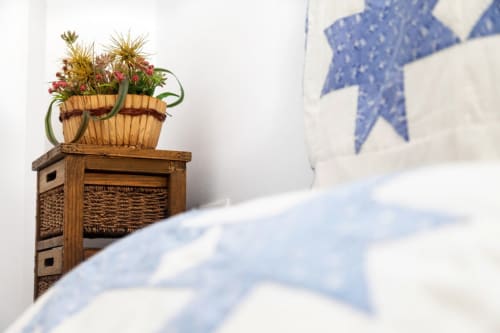 Unidad de almacenamiento en madera con maceta de mimbre tejido exhibiendo flores rojas y doradas en Barrosa Home apartment