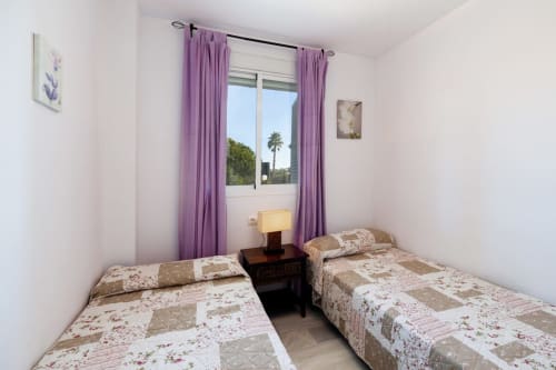Dormitorio doble con cortinas moradas y vistas a palmeras en el apartamento Barrosa Home, España