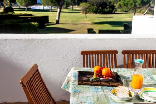 Terraza exterior en Barrosa Home con sillas de madera, mesa de patio con frutas frescas, jugos y cubiertos con vistas