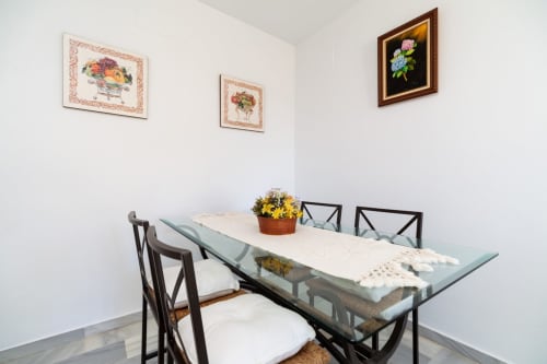 Comedor del apartamento Barrosa Home con cuadros florales enmarcados, mesa con flores amarillas y sillas negras