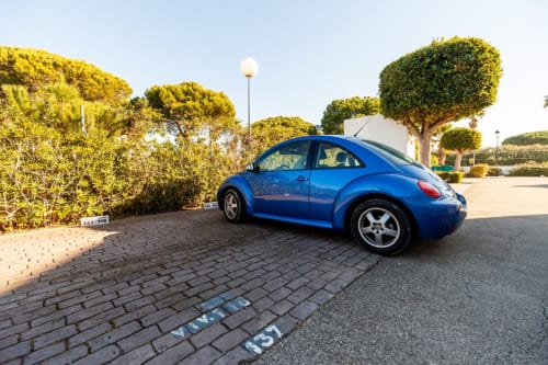 Escarabajo Volkswagen azul estacionado en el complejo residencial Barrosa Home en España, con setos bien cuidados y cielo despejado