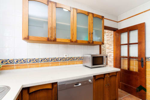 Cocina Barrosa con muebles de madera, encimera blanca, azulejos azules y dorados, y microondas en apartamento de España