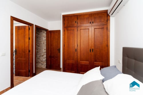 Dormitorio Barrosa con puertas de madera, ropa de cama blanca y cabecero gris