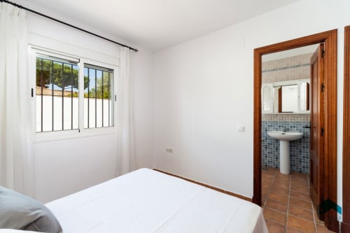 Dormitorio luminoso en Villa Maca de Barrosa Home con cama blanca, baño privado y acceso a terraza