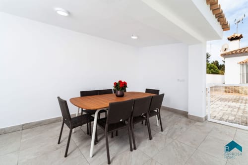 Comedor moderno de la villa Barrosa Home con mesa de madera, sillas negras y flores rojas con vista a la terraza