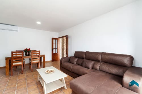 Amplia sala de estar en villa Barrosa Home con sofá de cuero marrón, mesa de comedor y piso de terracota