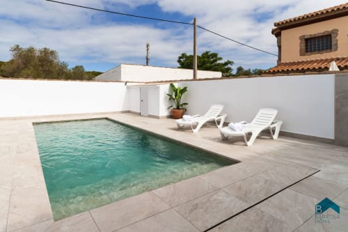 Villa Barrosa con piscina turquesa, tumbonas blancas y edificio de tejado terracota en España
